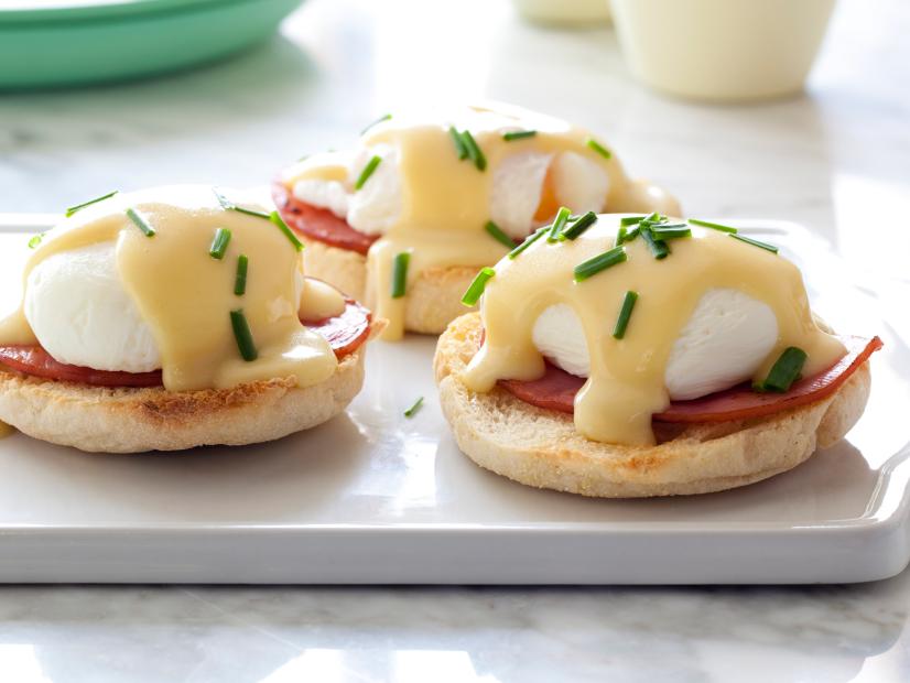 hollandaise sauce over three soft boiled eggs that sit on strips of bacon, all on top of English muffins